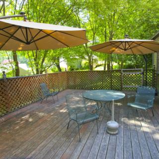 A sunny patio with outdoor furniture and umbrellas, surrounded by trees.