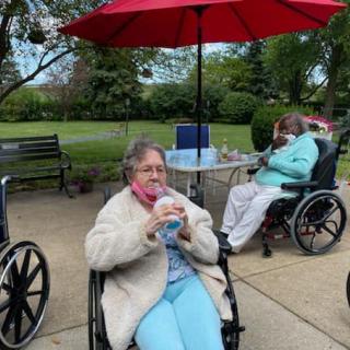 Seniors enjoying a sunny day at the park, sipping refreshments under a bright umbrella.