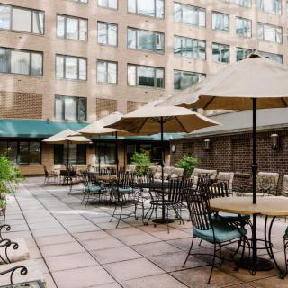 An outdoor patio area with tables, chairs, and umbrellas surrounded by a multi-story building.