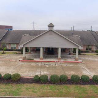 A view of a building entrance with a covered driveway and landscaped shrubs.