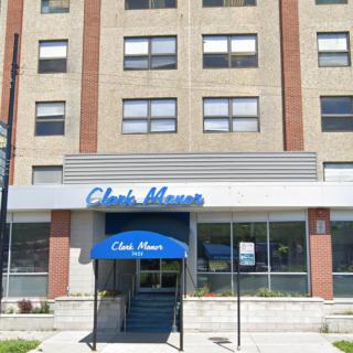 A street view of an apartment building with a blue awning over the entrance.