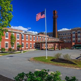 A large brick building with an American flag in the foreground under a clear blue sky.