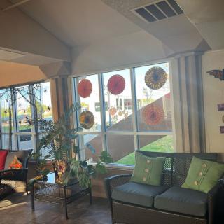 A cozy living room with large windows letting in sunlight, decorated with plants and comfortable seating.