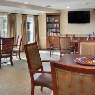 A cozy living room with several chairs and tables, a bookshelf, and a wall-mounted television.