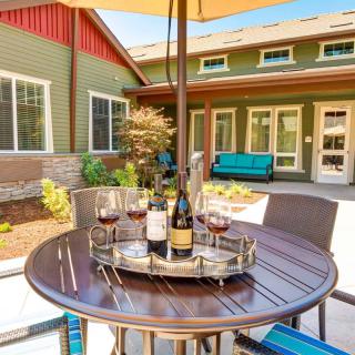 A cozy outdoor patio setup with a round table, wine bottles, and glasses under an umbrella on a sunny day.