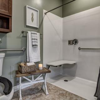 An accessible bathroom featuring a shower with grab bars and a folding seat, alongside a toilet and neatly arranged towels.