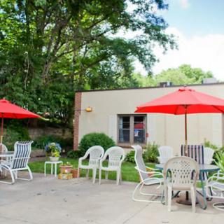 A patio with red umbrellas, white chairs, and tables surrounded by trees.