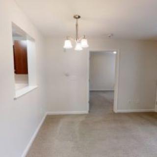 A dining area with white walls, carpet flooring, and a modern light fixture.