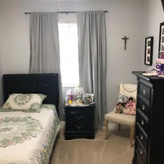A neatly organized bedroom with a bed, dresser, and chair adorned with decorative items.