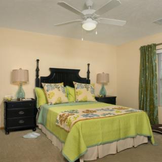 A cozy bedroom with green-themed bedding and curtains, featuring a dark wooden bed frame and matching nightstands, illuminated by table lamps.