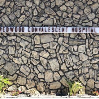 A sign for Redwood Convalescent Hospital set against a stone wall.