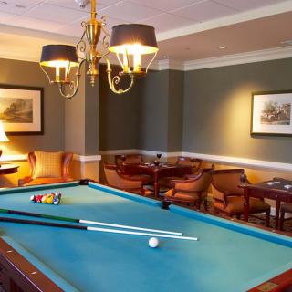 A cozy room featuring a pool table with cue sticks, seating area, and elegant lighting.