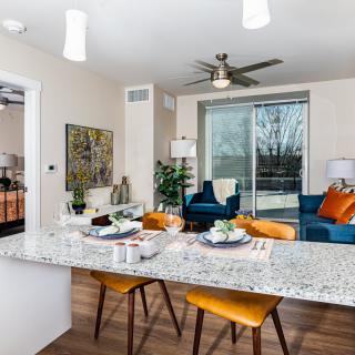 A modern open-concept living space featuring a kitchen with granite countertops, bar stools, and a cozy living area with vibrant decor.