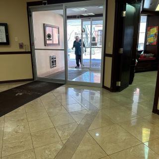 A person entering a building through glass doors into a tiled lobby.