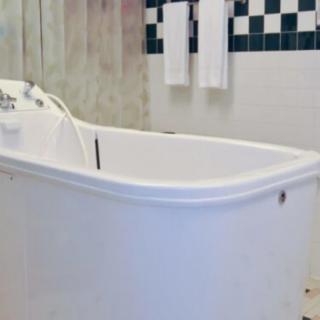 A bathroom featuring a white bathtub with checkered tile accents and towels hanging on the wall.