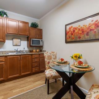 A cozy kitchen and dining area featuring wood cabinets, a small dining table set for two, and a decorative painting on the wall.