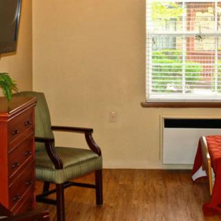 A cozy room with a wooden chair, dresser, and television near a window with blinds.