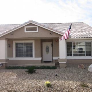 A single-story house with an American flag and a gravel front yard.