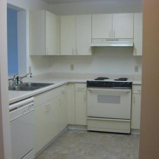 A small kitchen with white cabinets, a stove, and a sink.