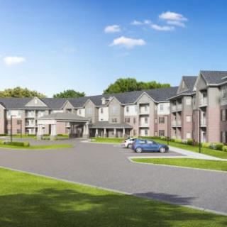 A modern suburban apartment complex with a parking area and green surroundings.