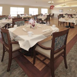 A well-arranged dining area with tables set for service, featuring white tablecloths and neatly arranged chairs.