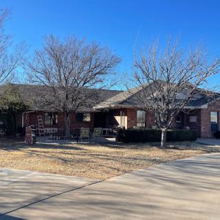 A suburban brick house with a driveway and leafless trees under a clear blue sky.