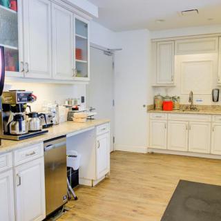 A modern kitchen with white cabinets, a coffee maker on the countertop, and a wooden floor.