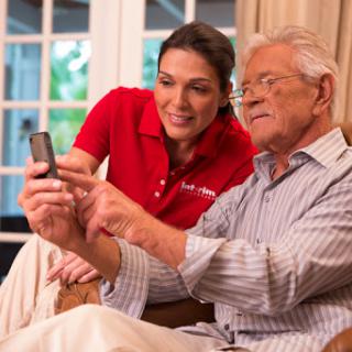 A caregiver helps an elderly man learn to use a smartphone.