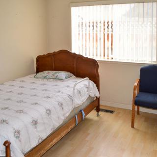 A small, minimalist bedroom with a single bed and a chair by the window.