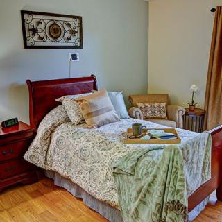 A cozy bedroom featuring a neatly made bed with patterned linens, a nightstand with a lamp, and comfortable seating.