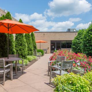 A serene outdoor garden space featuring comfortable seating and vibrant flowers under bright orange umbrellas.