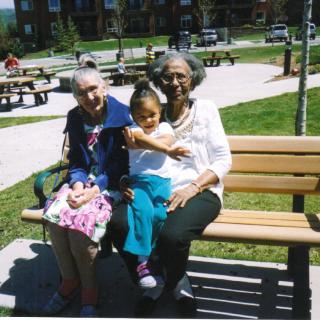 Three generations enjoying a sunny day in the park, sitting together on a bench.