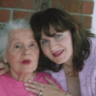 A middle-aged woman embraces an elderly woman in front of a brick wall.