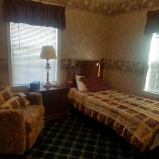 A cozy bedroom with a single bed, a lamp on a nightstand, and a chair by the window.
