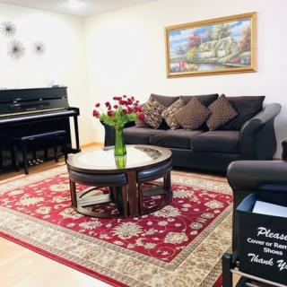 A cozy living room featuring a dark sofa with pillows, a piano, and a coffee table on an ornate red rug.