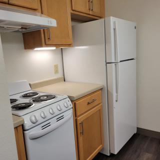 A compact kitchen with a stove, refrigerator, and wooden cabinets.