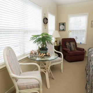 A cozy living room with a glass table, chairs, and a plant by the window.