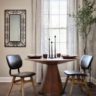A cozy dining area featuring a round wooden table with two modern chairs, accented by a decorative mirror and tall candles.