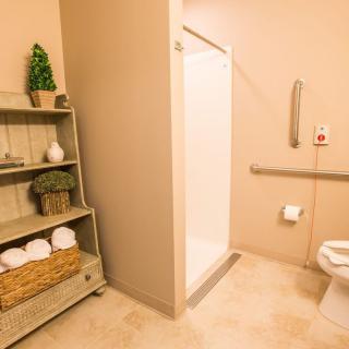 A well-organized, accessible bathroom with a shower, toilet, and neatly arranged towels on a shelf.