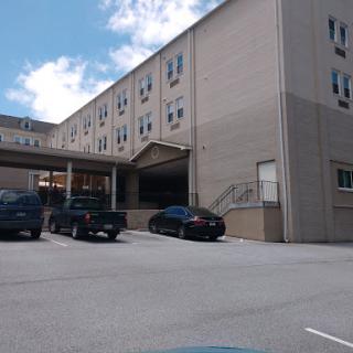 A view of a multi-story building with a parking lot in front, set against a partly cloudy sky.