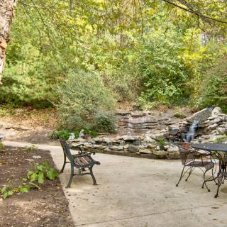 A serene patio with metal furniture overlooks a small waterfall surrounded by lush greenery.
