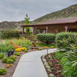 A beautifully landscaped garden with a winding pathway leading to a house, set against a mountainous backdrop.