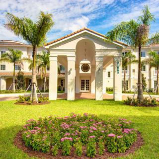 A beautifully landscaped residential complex with palm trees and vibrant flowers under a bright blue sky.