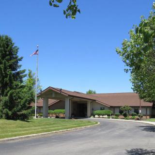 A single-story building with a driveway, surrounded by trees and grass under a clear blue sky.