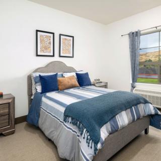 A cozy bedroom featuring a neatly made bed with striped bedding, complemented by blue and gray pillows, side tables, and wall art.