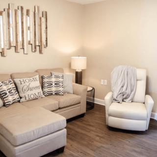 A cozy living room with a beige sofa, an armchair, and decorative mirror art on the wall.