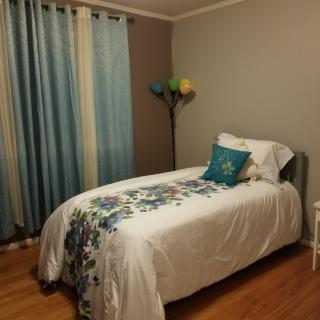 A neatly arranged bedroom with a single bed, decorative pillows, blue curtains, and a colorful lamp.