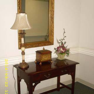 A decorative setup featuring an antique table with a lamp, flower arrangement, and a large mirror on the wall.