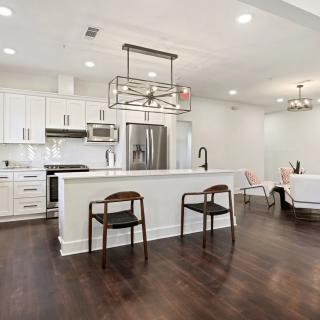 A modern open-concept kitchen with white cabinetry, hardwood floors, and stainless steel appliances.