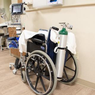 A wheelchair with an attached oxygen tank in a healthcare setting.